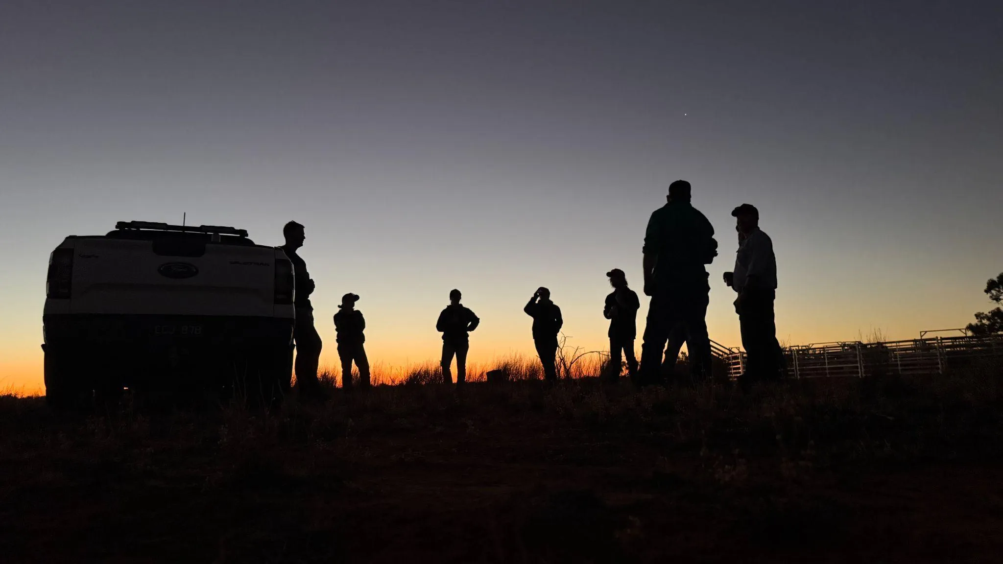 The Admedia team silhouetted against a sunset on location next to a vehicle, representing their collaborative approach to client work.