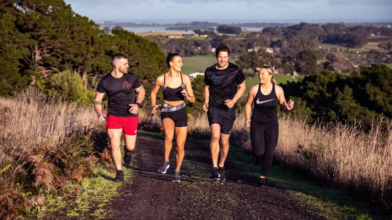 A group of 4 people running up a hill in exercise clothes on a sunny day