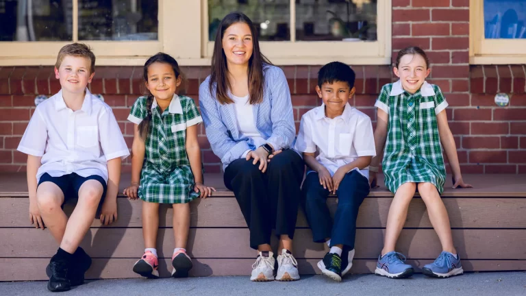 Admedia content creation: a teacher sitting with four primary school students on steps, reflecting the supportive environment of Catholic Education Sandhurst schools.