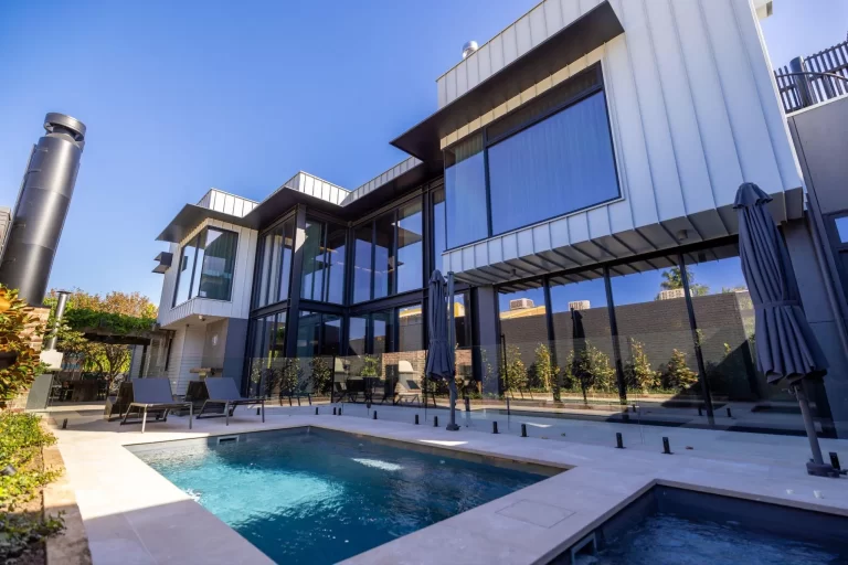 Modern two-story home with glass walls, contemporary architecture, swimming pool and outdoor entertaining area under clear blue sky
