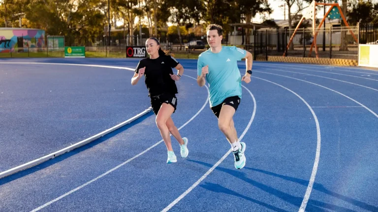 Man and woman running on a blue athletics track